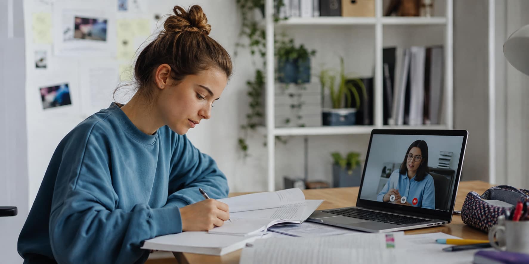 Dos chicas estudiando online con un ordenador, apuntes y cascos.